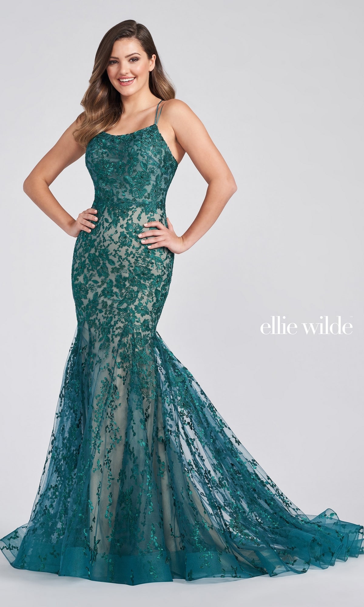 A woman models the Long Lace Mermaid Prom Dress with Strappy Back, featuring teal floral lace, thin straps, a fitted bodice, and a flared tulle skirt—showcasing the elegance of this open-back evening gown against a plain background.